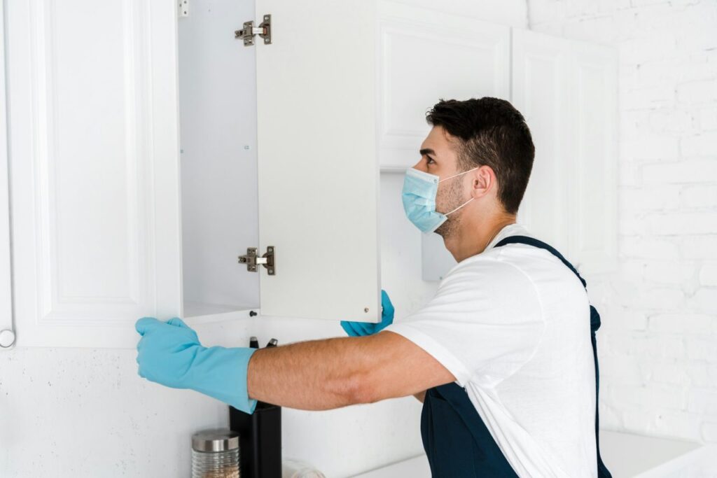 exterminator-in-uniform-looking-at-kitchen-cabinet.jpg